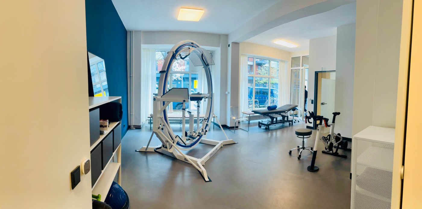 Der große Therapieraum mit dem Spacecurl vor der petrolfarbenen Wand.